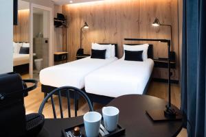 duas camas num quarto de hotel com uma mesa e cadeiras em Hôtel du Jardin des Plantes em Paris