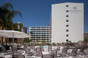 einem Pool mit Stühlen und einem Sonnenschirm und einem Gebäude in der Unterkunft Hotel Presidente 4 sup in Benidorm