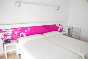 a bedroom with a white bed with a pink headboard at Hotel Agades in San José