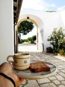una persona sosteniendo un plato con una taza de café y un trozo de pastel en Masseria Marico, en Castellaneta