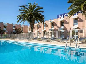a swimming pool in front of a building with palm trees at Novotel Perpignan Nord Rivesaltes in Rivesaltes