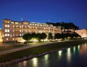 ein großes Gebäude neben einem Fluss in der Nacht in der Unterkunft Hotel Sacher Salzburg in Salzburg
