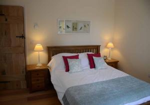 een slaapkamer met een bed met rode kussens en 2 lampen bij Raleigh Barn in West Putford