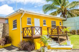 a yellow house with a balcony and palm trees at Adulo Apartments in Bridgetown