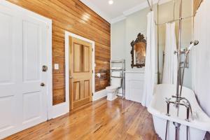La salle de bains est pourvue d'une baignoire blanche et d'un mur en bois. dans l'établissement NOLA Cottage, à La Nouvelle-Orléans