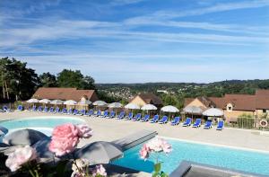 un complexe doté d'une piscine avec des chaises longues et des parasols dans l'établissement Résidence Odalys - Les Coteaux de Sarlat, à Sarlat-la-Canéda