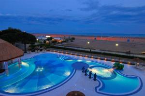 een zwembad 's nachts met de oceaan op de achtergrond bij Ashanti Aparthotel Wellness&Spa in Bibione