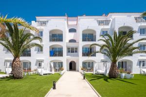 a white building with palm trees in front of it at FERGUS Style Carema Beach in Cala en Bosc