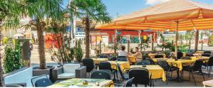 ein Restaurant mit Tischen, Sonnenschirmen und Palmen in der Unterkunft Hotel Blumenstein Self-Check In in Frauenfeld