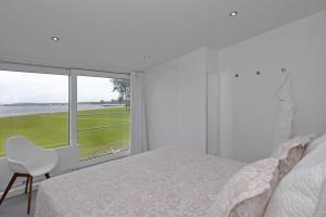 Dormitorio blanco con ventana, cama y silla en Havenweg 12 - direct aan het Veerse Meer, en Kamperland