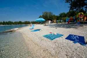 a beach with chairs and an umbrella and a playground at Maistra Camping Valkanela Mobile homes in Funtana