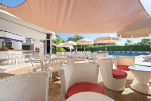 un patio con sillas blancas, mesas y sombrillas en azuLine Hotel Llevant, en San Antonio