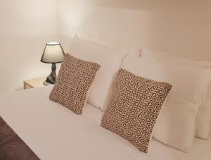 Una cama con almohadas blancas y una lámpara en una mesa. en Like-home Sea View Apt, en Carcavelos