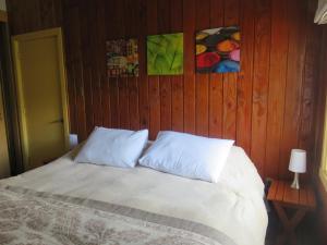 a bed with two white pillows and a wooden wall at Cabañas Donde La Oma in Villarrica