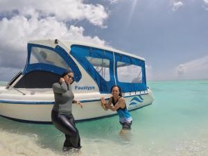 two women standing in the water next to a boat at Salt Beach Hotel in Maafushi