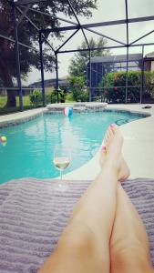 una donna sdraiata di fronte a una piscina con un bicchiere di vino di Maya's Villa a Haines City