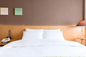 a bed with white sheets and a phone on a table at Matsumoto Marunouchi Hotel in Matsumoto