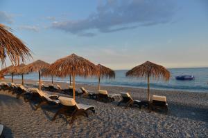 um grupo de cadeiras e guarda-sóis de palha numa praia em Hotel Villa MIKI em Bordighera