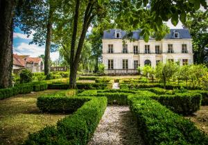 un jardin en face d'une maison blanche avec des arbres et des buissons dans l'établissement Château de Picheny - B&B Esprit de France, à Picheny