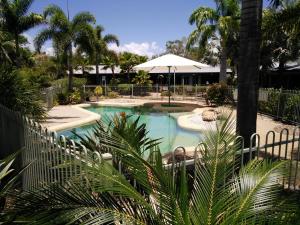 a large swimming pool with an umbrella and palm trees at Capricorn Motel & Conference Centre in Rockhampton