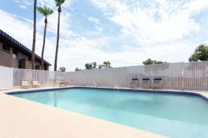 einen Pool mit Stühlen, einem Zaun und Palmen in der Unterkunft Super 8 by Wyndham Chandler Phoenix in Chandler