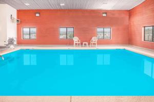 une grande piscine avec deux chaises devant un mur de briques dans l'établissement Super 8 by Wyndham Van Buren/Ft. Smith Area, à Van Buren