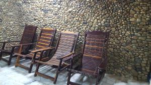 3 sillas de madera sentadas junto a una pared de piedra en Ratmanee House, en Kanchanaburi