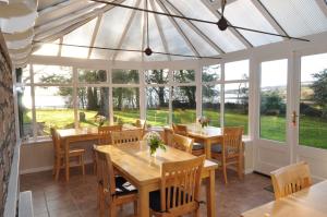 un salón acristalado con mesas, sillas y ventanas en Kiltearn Guest House, en Evanton