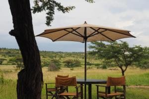 einen Tisch mit 2 Stühlen und einem Sonnenschirm in der Unterkunft Basecamp Wilderness in Naboisho