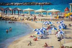 una playa con sombrillas y gente en el agua en The New Port Hotel TLV, en Tel Aviv