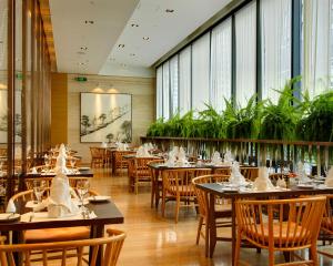uma sala de jantar com mesas, cadeiras e plantas em Marco Polo Parkside, Beijing em Pequim