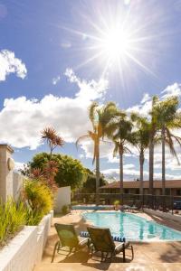 a pool with two lawn chairs and palm trees at Sunseeker Motor Inn in Batemans Bay