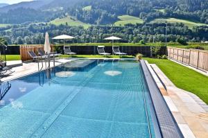 a swimming pool with chairs and umbrellas in a backyard at Hotel Druschhof in Schladming
