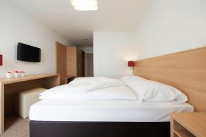 a bedroom with a bed with white sheets and a television at Sternen Hotel Wolfurt in Bregenz