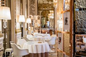 a restaurant with white tables and chairs and a mirror at Le Meurice – Dorchester Collection in Paris