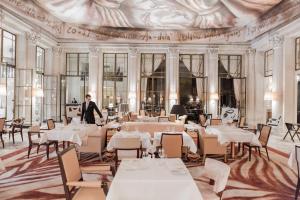 a man standing in a restaurant with tables and chairs at Le Meurice – Dorchester Collection in Paris