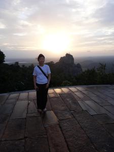 a woman standing on top of a mountain with the sun in the background at Hewage Resort in Anuradhapura
