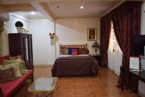 a bedroom with a bed and a couch and a tv at The Saint Joseph Residential Suites in Lucena