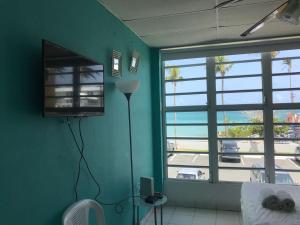 a room with a green wall with a television and windows at Coco Mar Oceanview Studios in San Juan