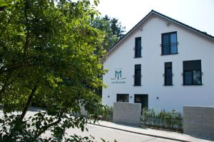 a white building with black windows and a tree at Hotel Am Moosrain Garni in Eitting