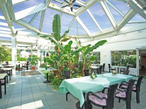 a conservatory with tables and chairs and plants at Hotel Maromme in Norderstedt