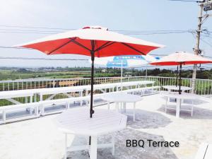 two white tables and an umbrella on a balcony at Sunset Hill Bise in Motobu