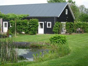 ein schwarzes Haus mit einem Teich davor in der Unterkunft B&B Oostzomerland in Mijnsheerenland