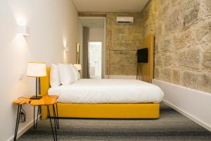 1 dormitorio con cama amarilla y pared de piedra en BO - Álvares Cabral GuestHouse, en Oporto