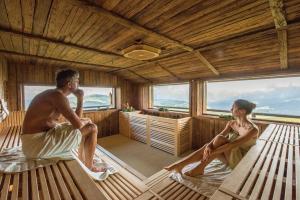 Ein Mann und eine Frau sitzen in einer Sauna in der Unterkunft Hotel Goldknopf in Alpe di Siusi