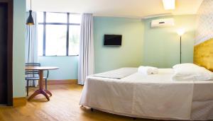 a bedroom with a bed and a table and a window at Pontual Hotel in Bocaiúva