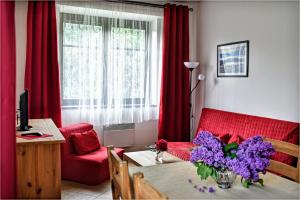 ein Wohnzimmer mit roten Vorhängen und einem Tisch mit lila Blumen in der Unterkunft Apartmánový Dům Pasťák in Loučná nad Desnou