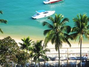a white boat in the water next to palm trees at Hotel Itapemar - Ilhabela in Ilhabela