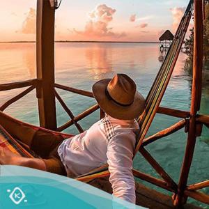 a man in a hat sitting on a swing at Villas Karalv in Bacalar
