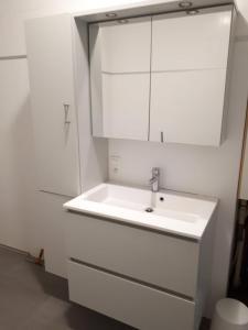 ein Badezimmer mit einem weißen Waschbecken und weißen Schränken in der Unterkunft Residentie Koen in Ostende